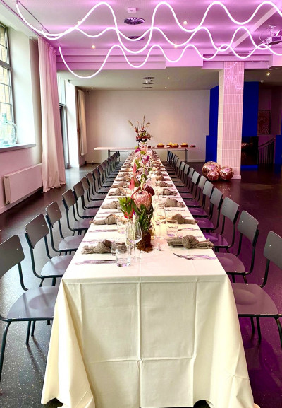 Lange gedeckte Tafel, an der Decke leuchtet eine pinke Lichtinstallation