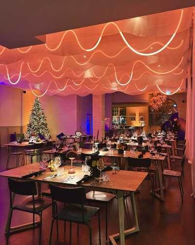 Blick in den großen Eventraum, Mehrere Tische, ein großer Weihnachtsbaum und passende rote Beleuchtung